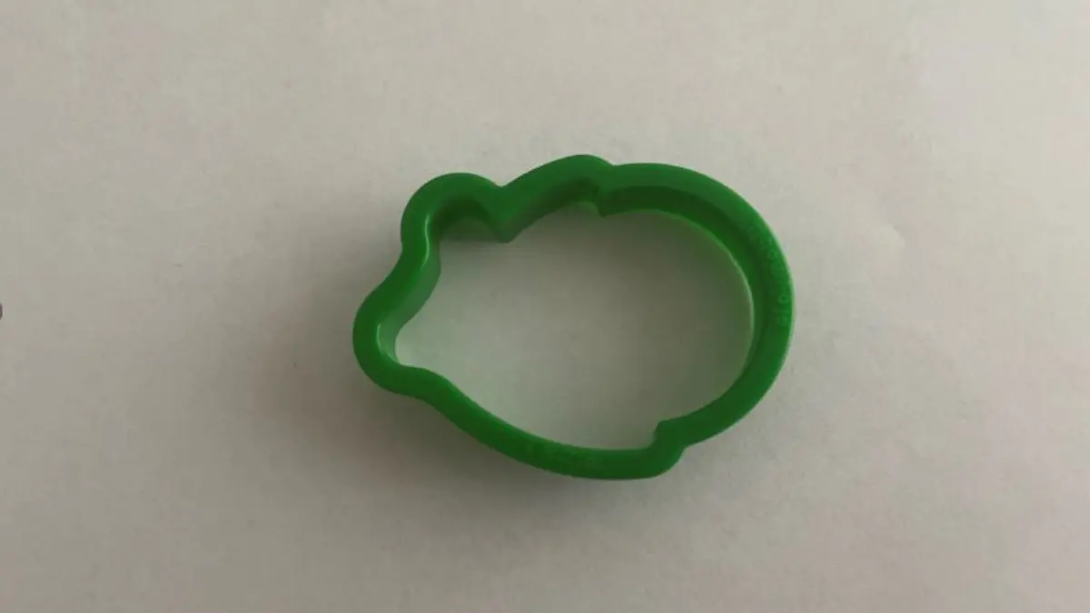 Grüne Plätzchenform liegt auf weißem Blatt Papier.