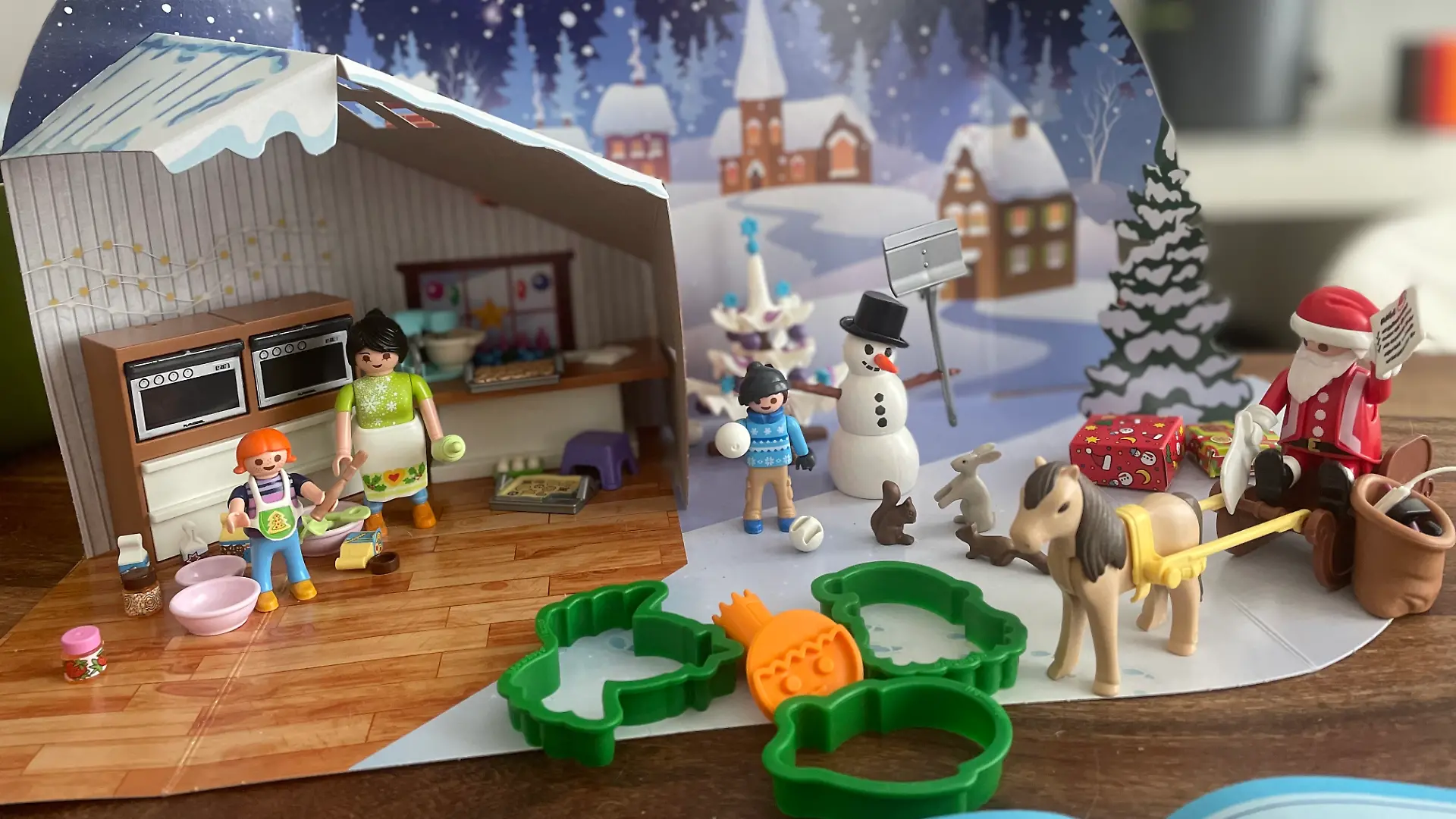 Figuren und Zubehör des Playmobil Back-Adventskalenders aufgestellt vor dem Papp-Hintergrund. 