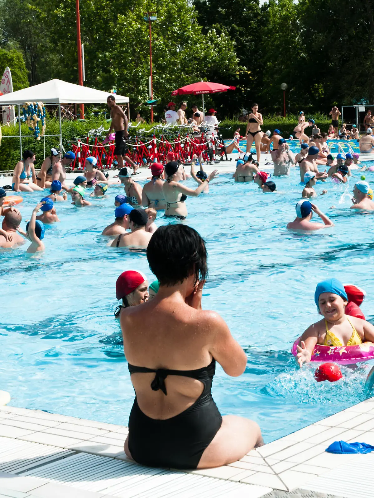 "Bologna, Italy - July 1, 2012: Adulta and families with children refreshing themself and having fun in a crowded swimming pool near Bologna (Italy). It's a sunny day, during a very hot summer."