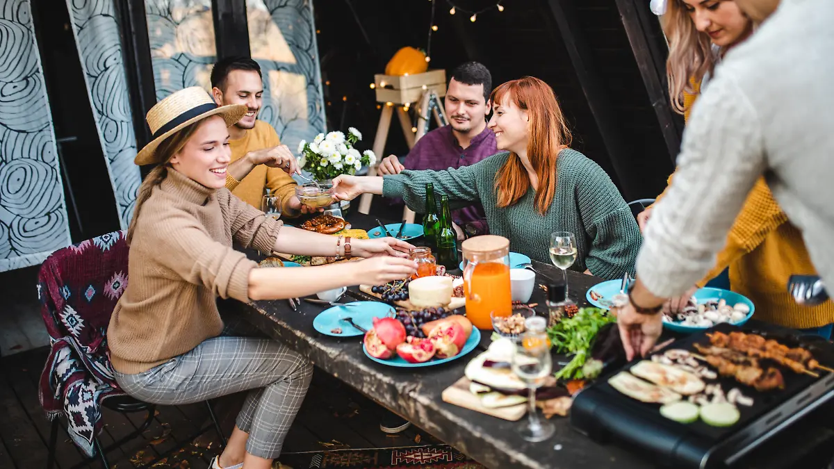 Group of six people preparing and eating food together out on the porch