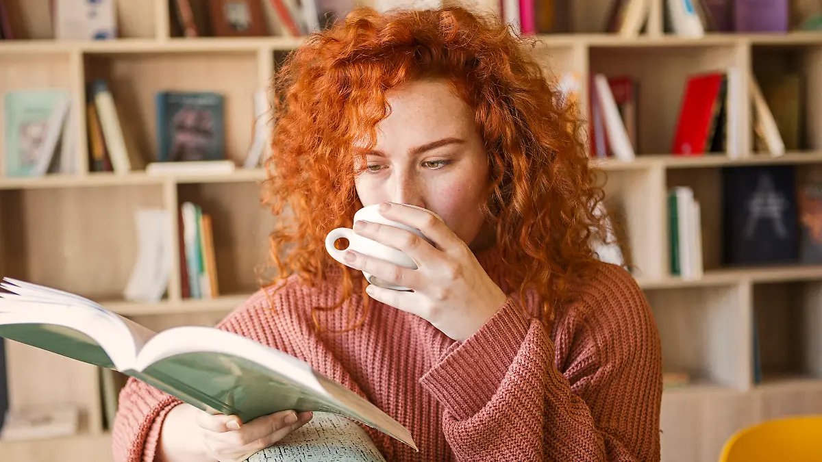 Eine junge Frau trinkt ein Heißgetränk und liest ein Buch.