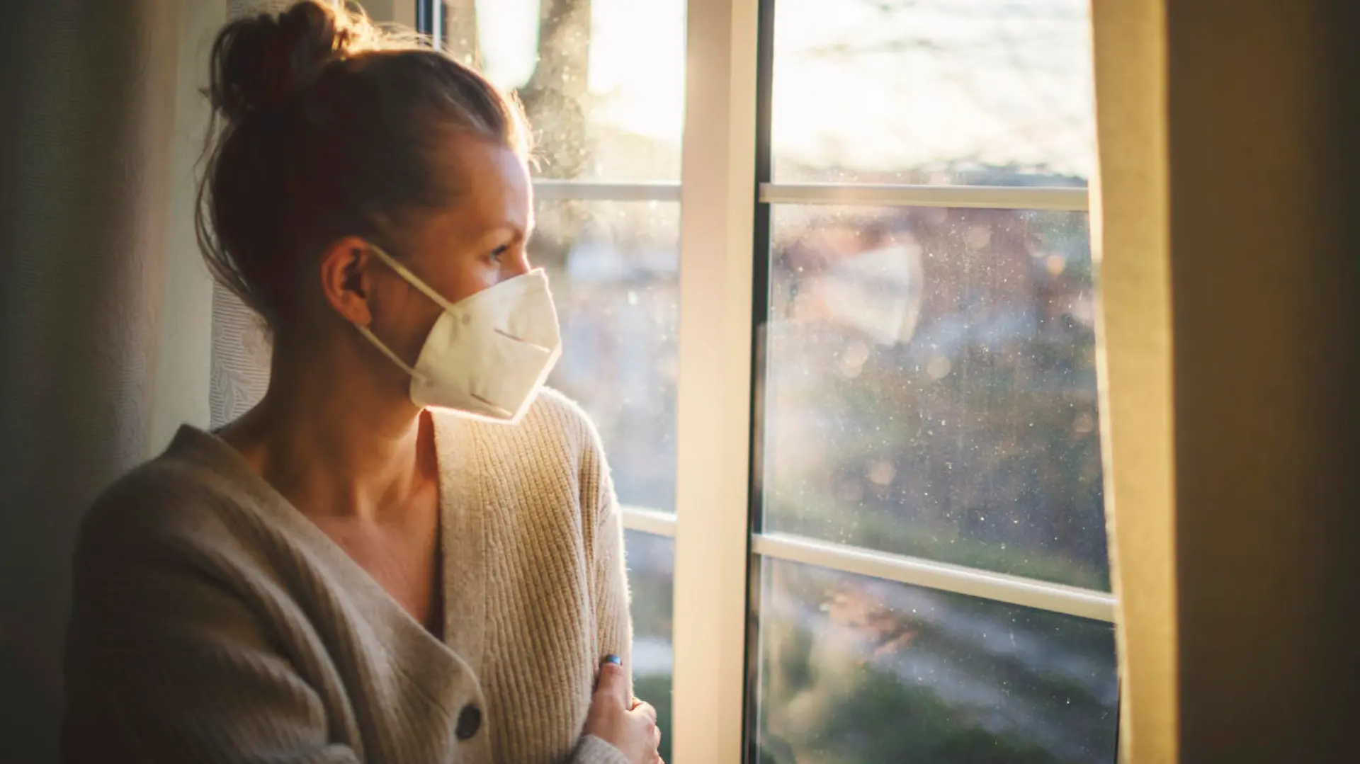 Pretty woman in quarantine with FFP2 mask, looks out the window