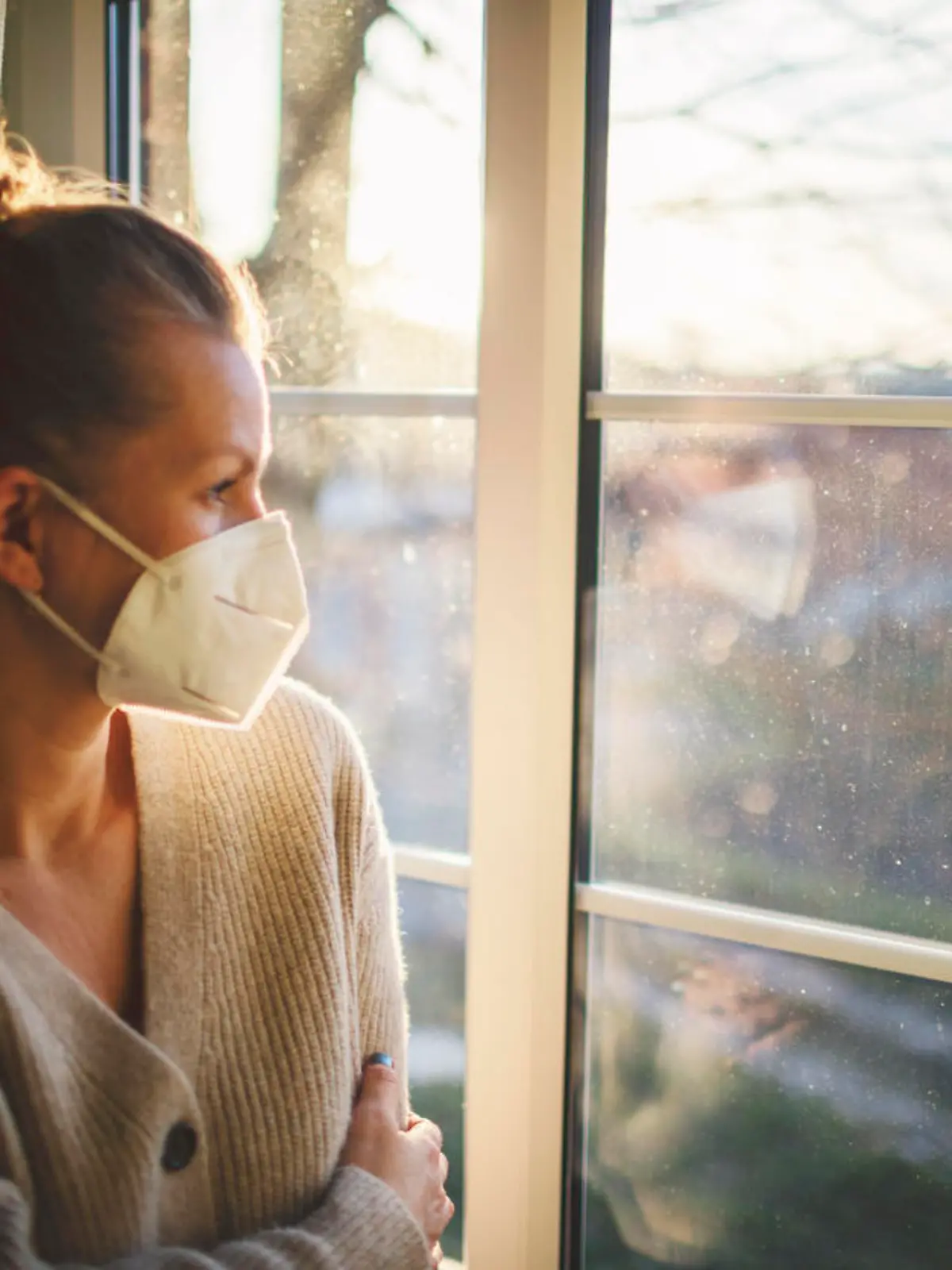 Pretty woman in quarantine with FFP2 mask, looks out the window