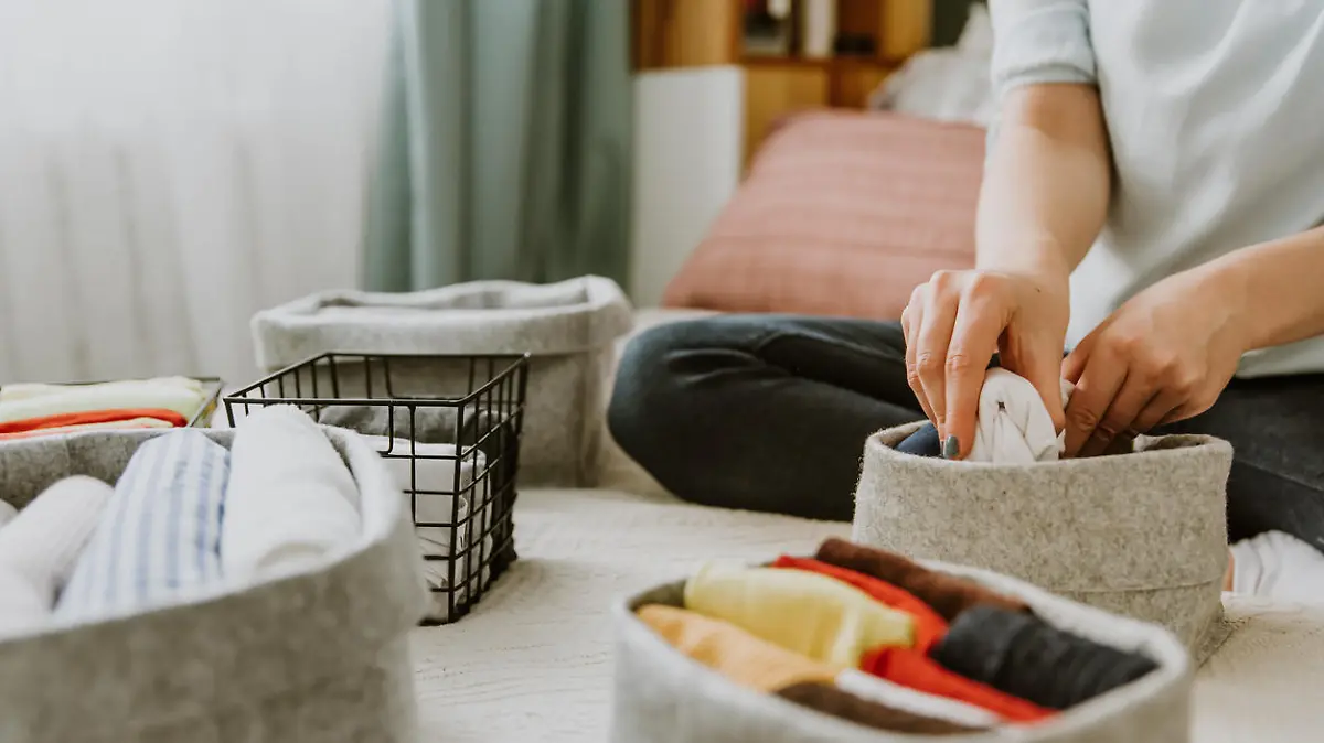 Woman organizing clothes in wardrobe, putting shirts in boxes. Concept of order, minimalist closet, japanese t-shirt folding system and clothes storage