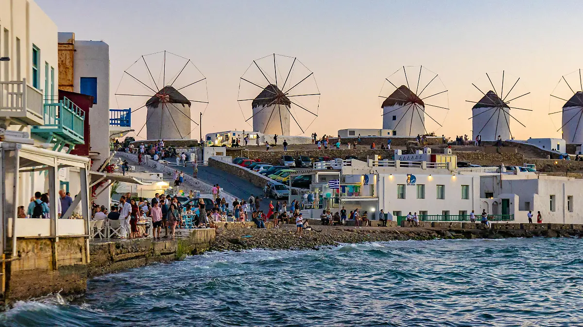 The iconic windmills of Mykonos island as seen from Little Venice with tourists at the bars, cafes and restaurants. Mykonos is an island in Greece in the Aegean sea. There are 16 windmills on the island, 5 of them above Chora, the main town in the island. The windmills were built in the 16th century from the Venetians but their constructions continued until the 20th century. Sunset with people at the windmills in Mykonos. Tourists enjoy a beautiful sunset during the magic hour at Mykonos island in Greece. The Greek island of Myconos is a popular glamorous Mediterranean travel destination for holidays in the Cyclades, Aegean Sea with the iconic whitewashed buildings, the sandy beaches and famous party at the beach bars. The tourism and travel industry had a negative impact in the business and local economy sector due to the Covid-19 Coronavirus pandemic. Mykonos island, Greece(Photo by Nicolas Economou/NurPhoto)
