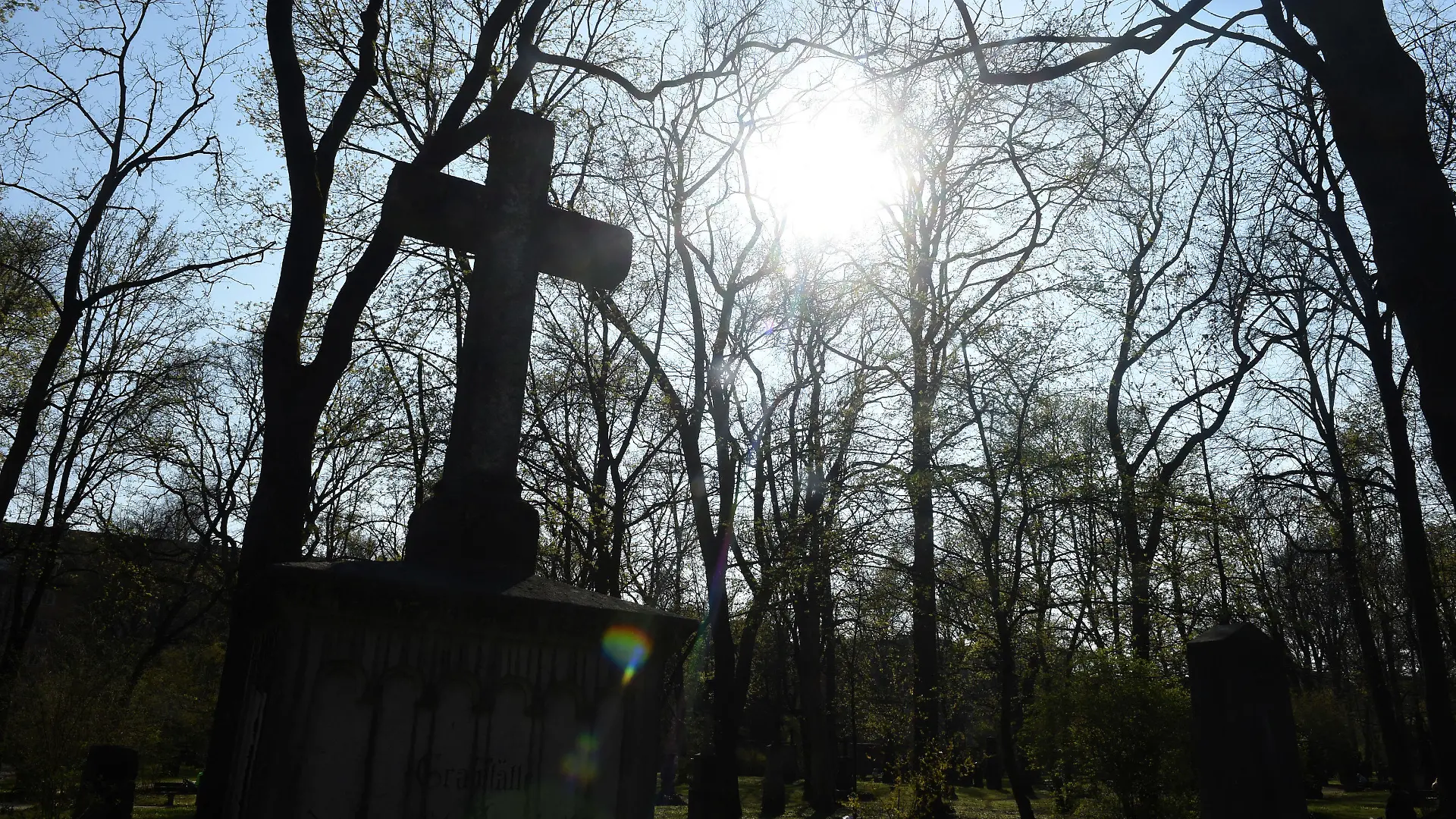 ARCHIV - 07.04.2020, Bayern, München: Die Sonne scheint hinter den Bäumen und eine Kreuz des Alten Nördlichen Friedhof. In Bayern feiern die evangelischen Christen Buß- und Bettag. Der Tag ist zwar kein gesetzlicher Feiertag mehr, Unterricht an den Schulen gibt es trotzdem nicht. Foto: Felix Hörhager/dpa +++ dpa-Bildfunk +++