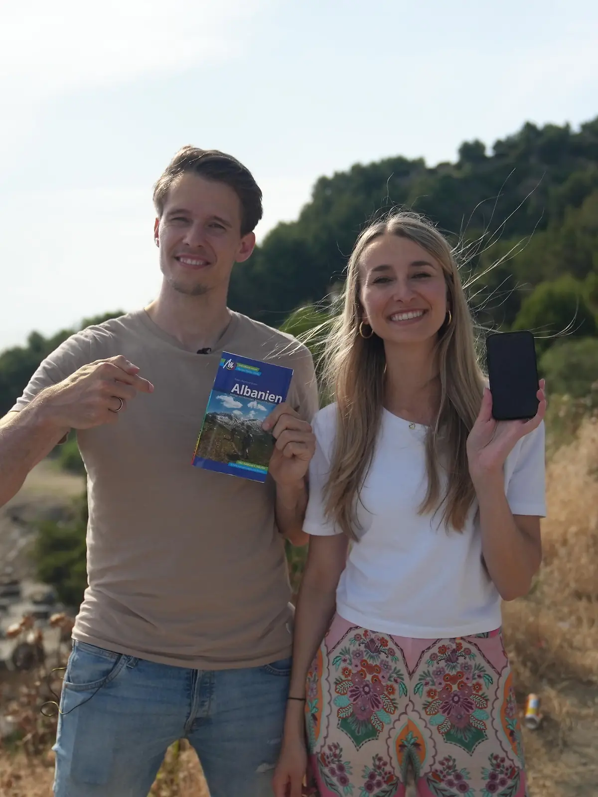 Frau mit Handy in der Hand, Mann mit einem Reiseführer am Strand in Albanien