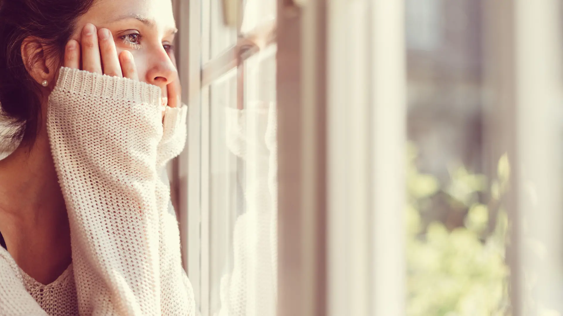 Frau schaut einsam aus dem Fenster. 