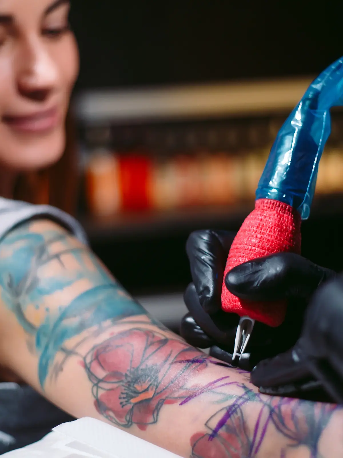 Frau wird ein buntes Tattoo auf dem Arm gestochen
