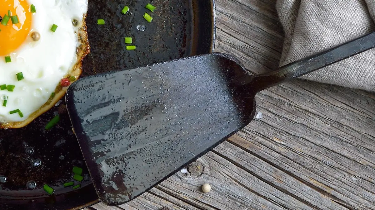 Pfanne mit zwei Spiegeleiern steht auf dem Herd mit einem schwarzen Plastik-Pfannenwender an der Seite.
