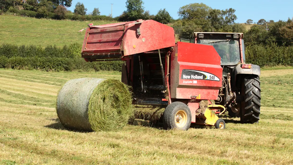 Ein Landwirt ist mit einer Rundballenpresse auf einem Feld in Großbritannien unterwegs.