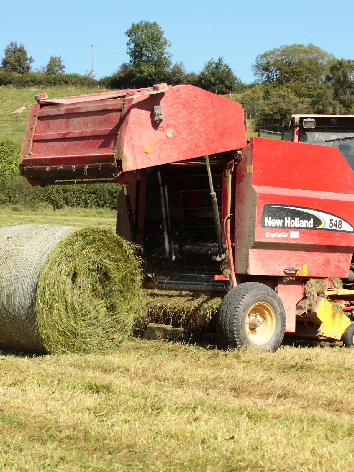 Ein Landwirt ist mit einer Rundballenpresse auf einem Feld in Großbritannien unterwegs. 