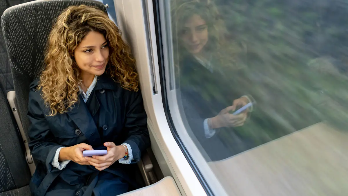 Beautiful woman traveling by train looking at the view while texting on smartphone - High angle view