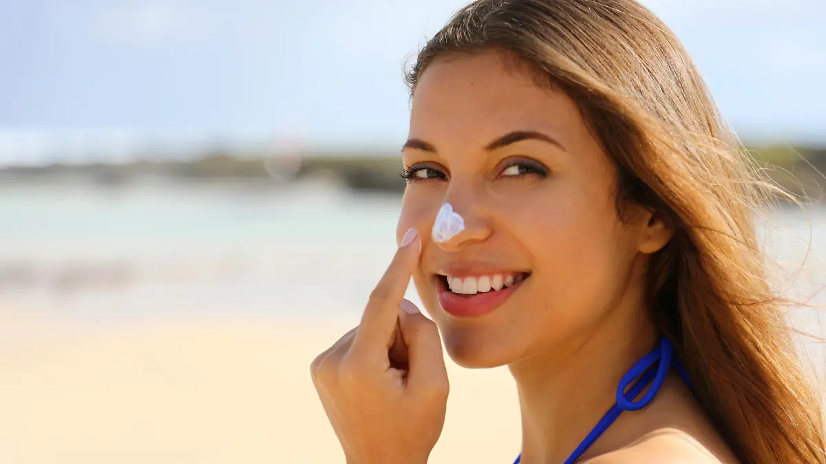 Close up young beautiful woman applying sun cream protection on her nose on the beach. Suntan lotion woman applying sunscreen solar cream.