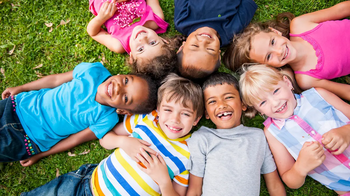 Mehrere lachende Kinder liegen auf Rasen im Kreis.