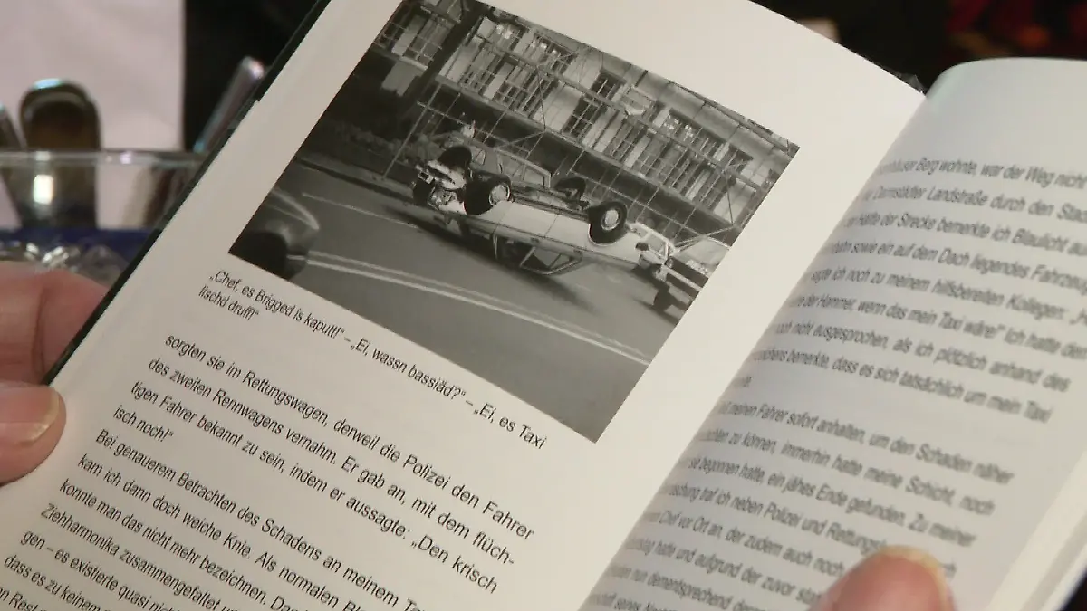 Nahaufnahme des aufgeschlagenen Buches, ein Bild mit einem Taxi, welches auf dem Dach liegt sticht aus der Buchseite hervor.