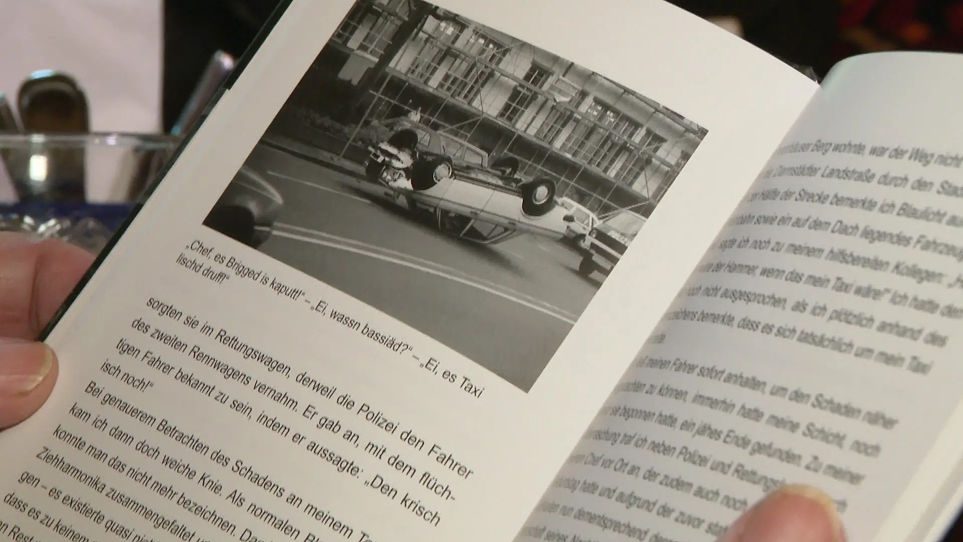 Nahaufnahme des aufgeschlagenen Buches, ein Bild mit einem Taxi, welches auf dem Dach liegt sticht aus der Buchseite hervor.