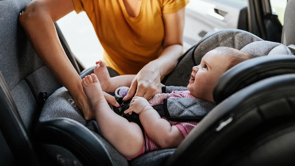 Mother putting baby girl in baby car seat.