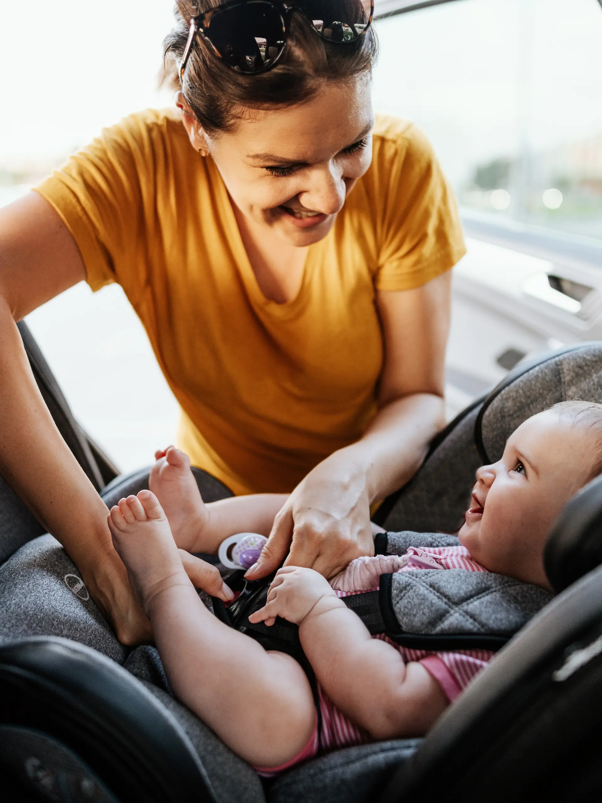 Mother putting baby girl in baby car seat.