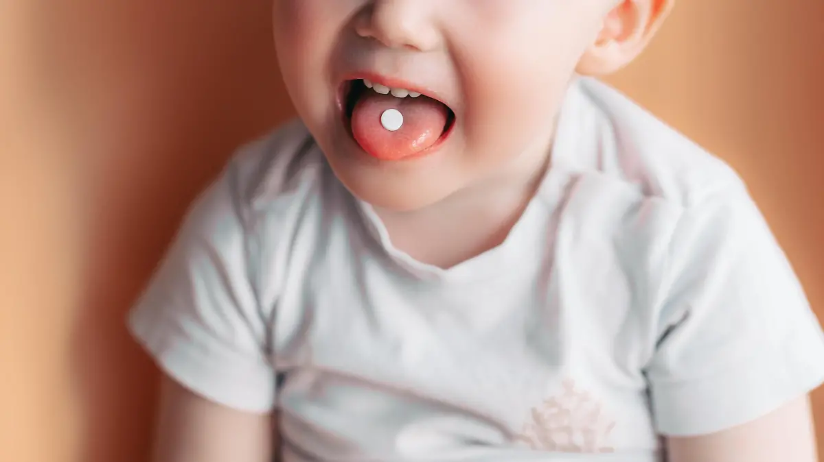 Selective focus at a white pill on a tongue of small toddler baby boy.