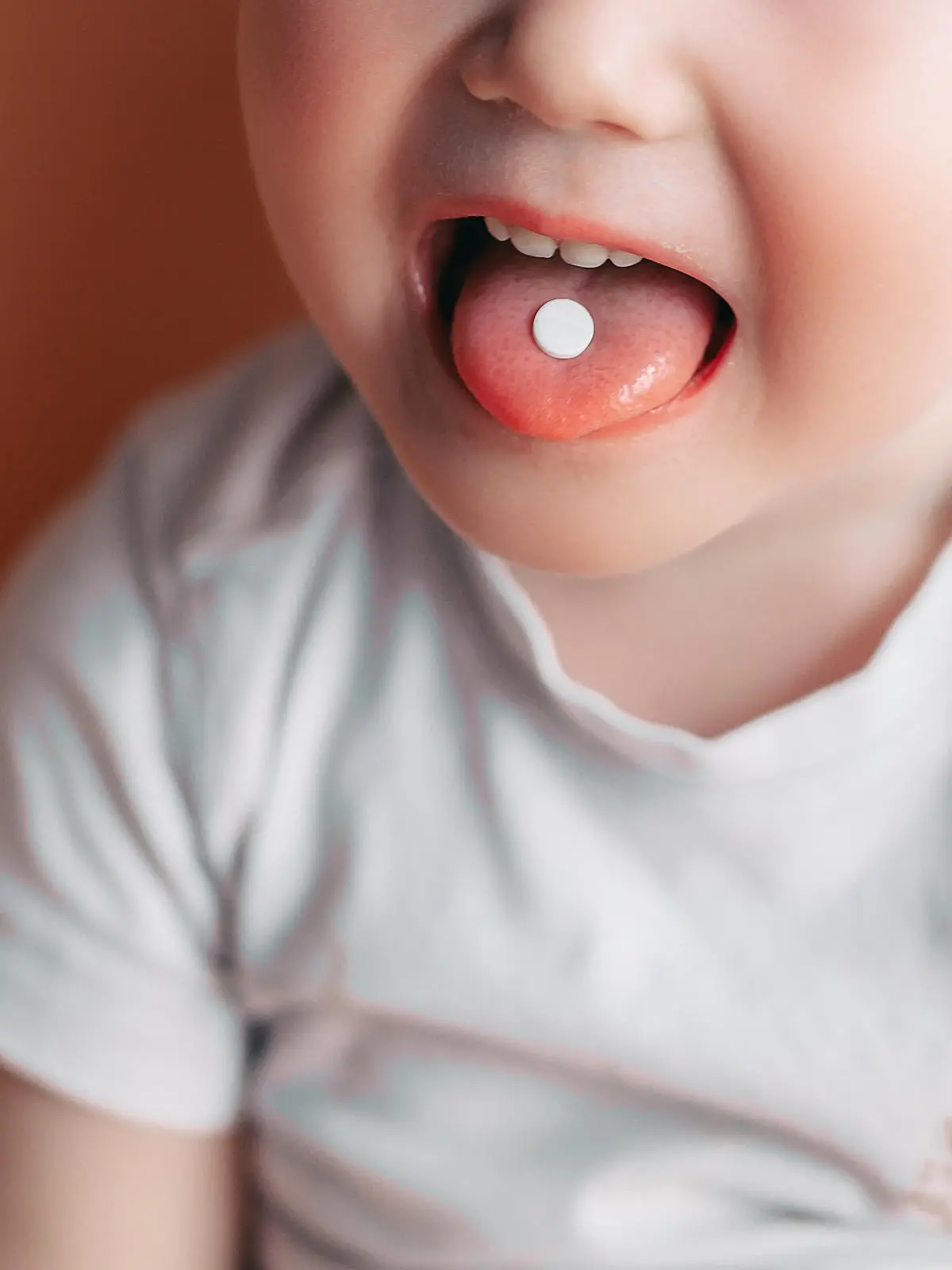 Selective focus at a white pill on a tongue of small toddler baby boy.
