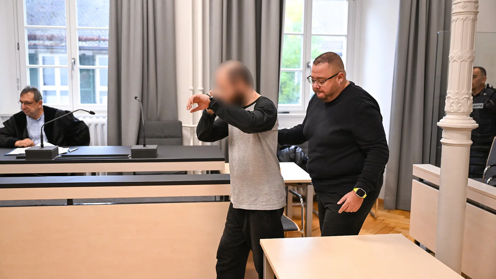 Ein Mann betritt in Handschellen den Gerichtssaal. Dem Beschuldigten wird vorgeworfen, eine Vierjährige im Supermarkt mit einem Messer attackiert zuhaben. Der Mann wird von Justizmitarbeitern hineingeführt.