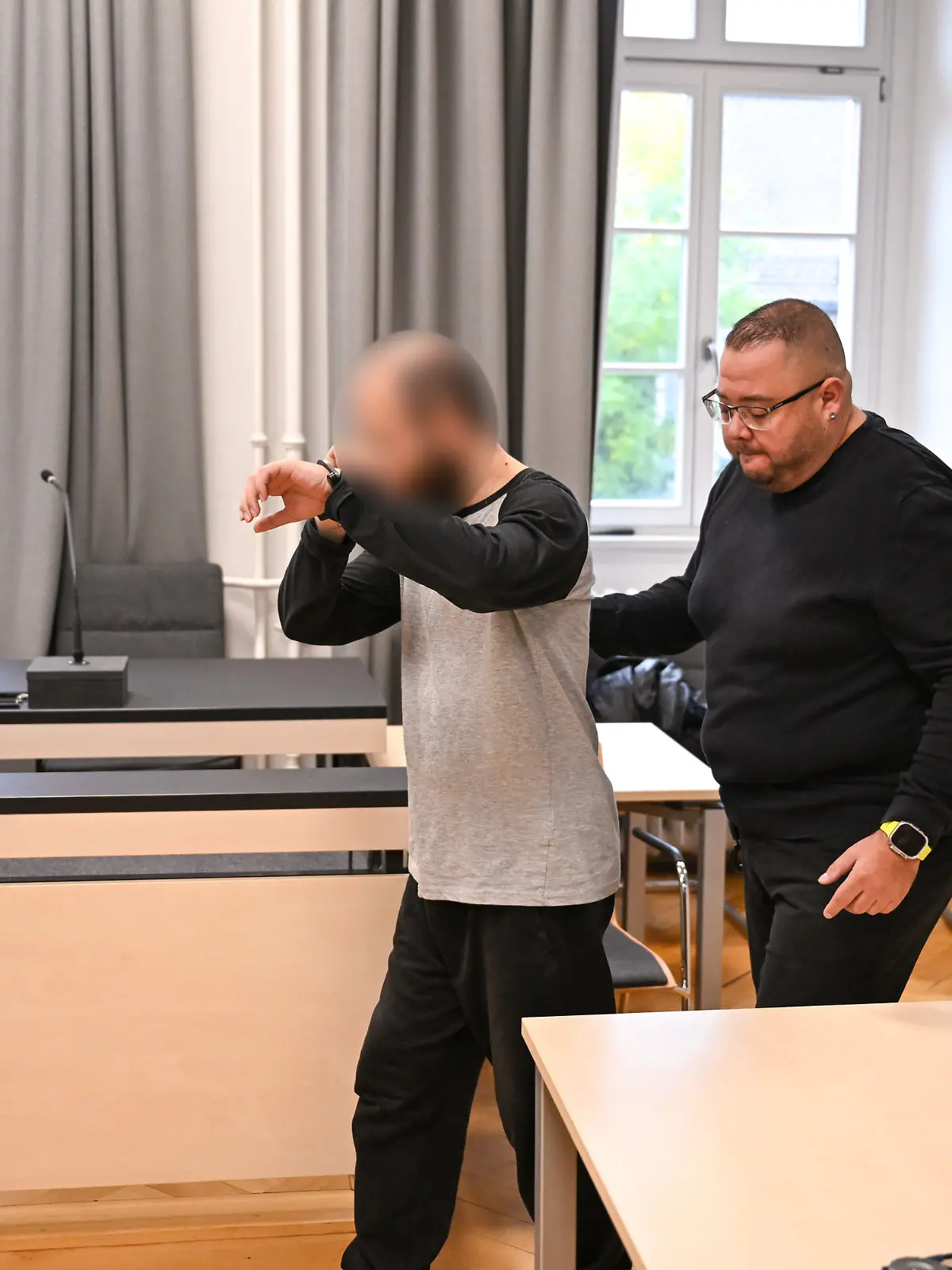 Ein Mann betritt in Handschellen den Gerichtssaal. Dem Beschuldigten wird vorgeworfen, eine Vierjährige im Supermarkt mit einem Messer attackiert zuhaben. Der Mann wird von Justizmitarbeitern hineingeführt.