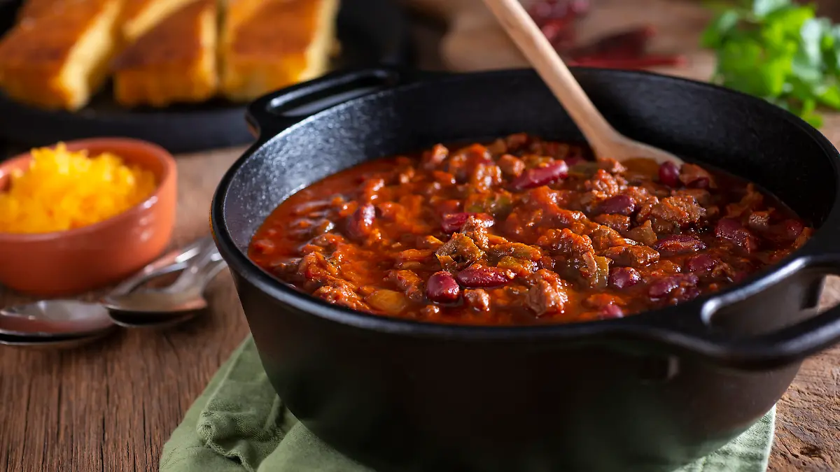 Ein gusseiserner Bräter mit Chili con carne steht auf einem Tisch.