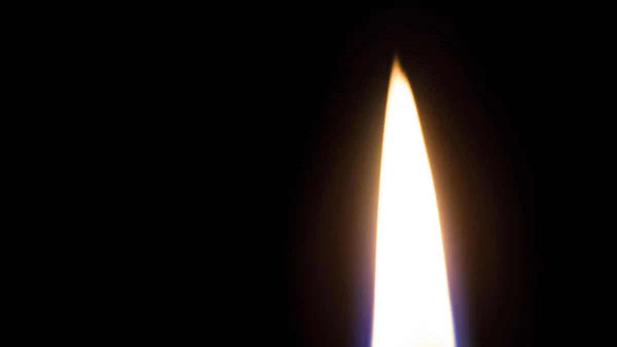A closeup of a white candle burning in the dark. The flame is blue at the base. Isolated on Black