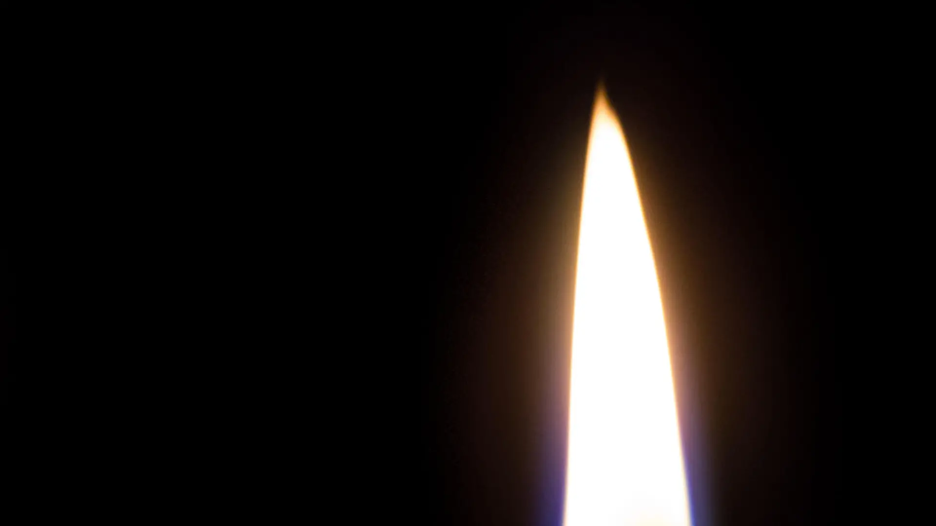 A closeup of a white candle burning in the dark. The flame is blue at the base. Isolated on Black