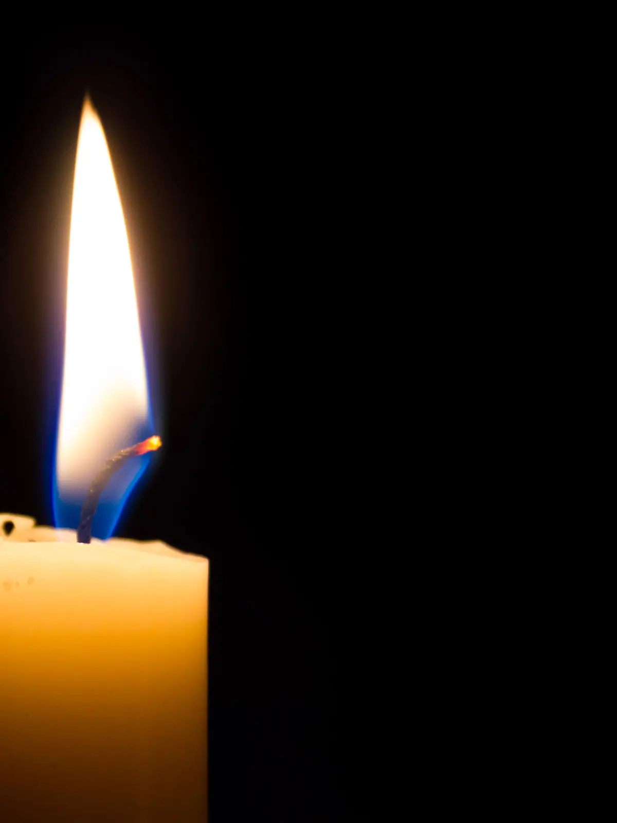 A closeup of a white candle burning in the dark. The flame is blue at the base. Isolated on Black