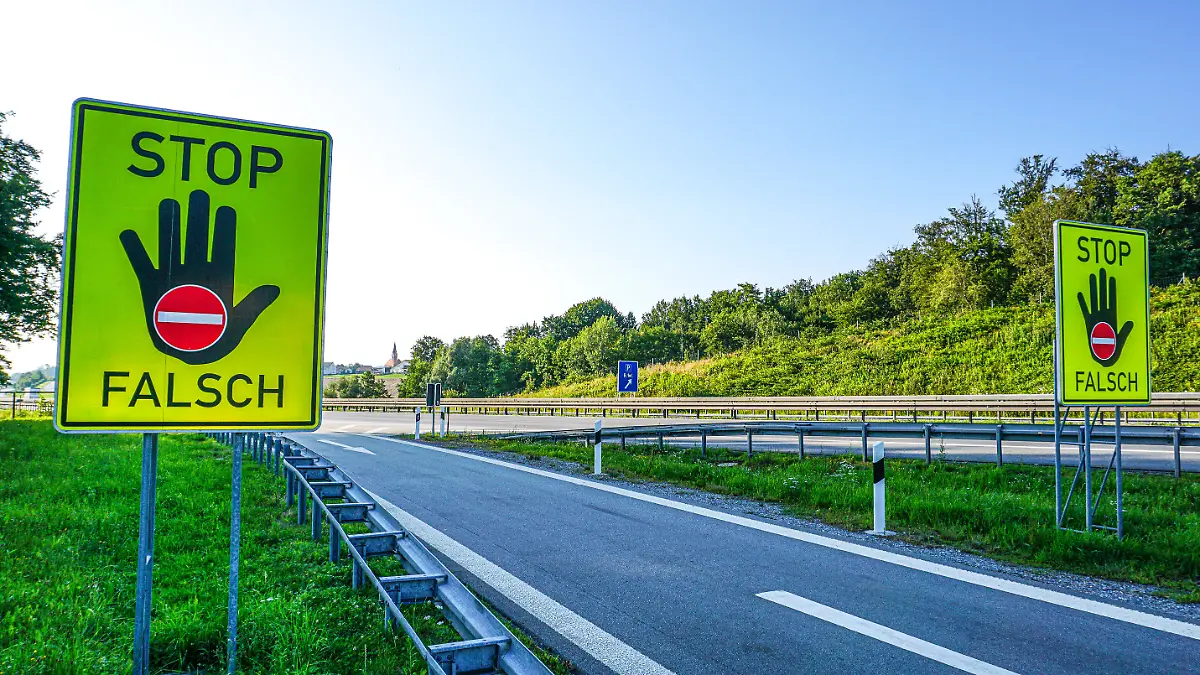 An einer einer Autobahn stehen Warnschilder für einen eventuellen Geisterfahrer, Falschfahrer. Auf den Verkehrsschildern wird darauf hingewiesen, dass der Fahrer in den Gegenverkehr fährt. Auf dem Neongelben Schild steht Stop, Falsch, mit einer warnenden Hand und dem Durchfahrtverboten Symbol.