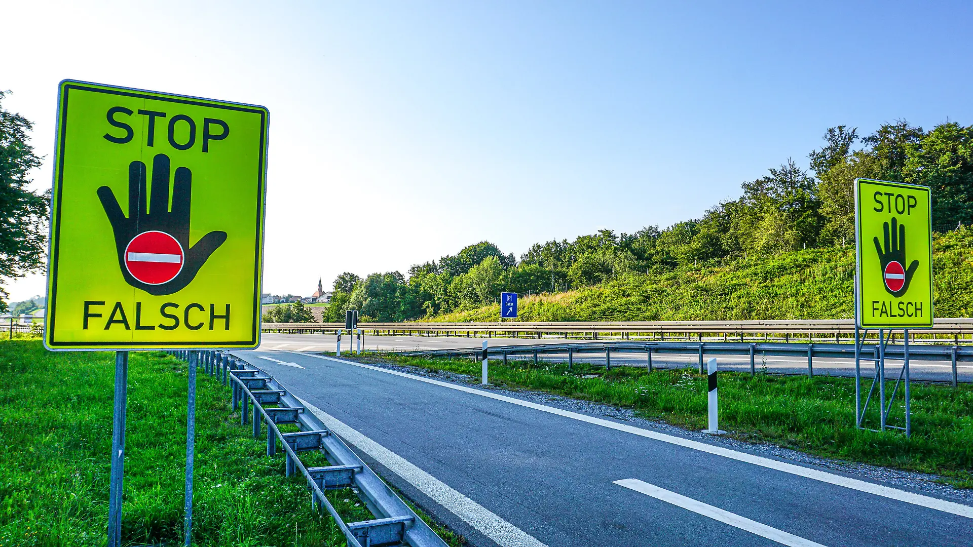 An einer einer Autobahn stehen Warnschilder für einen eventuellen Geisterfahrer, Falschfahrer. Auf den Verkehrsschildern wird darauf hingewiesen, dass der Fahrer in den Gegenverkehr fährt. Auf dem Neongelben Schild steht Stop, Falsch, mit einer warnenden Hand und dem Durchfahrtverboten Symbol.