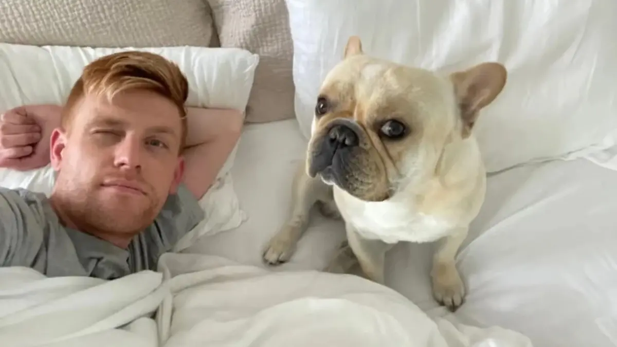 Auf dem Bild sind Michael C. und seine Hündin Ash zu sehen, wie sie im Bett liegen. Beide schauen in die Kamera.