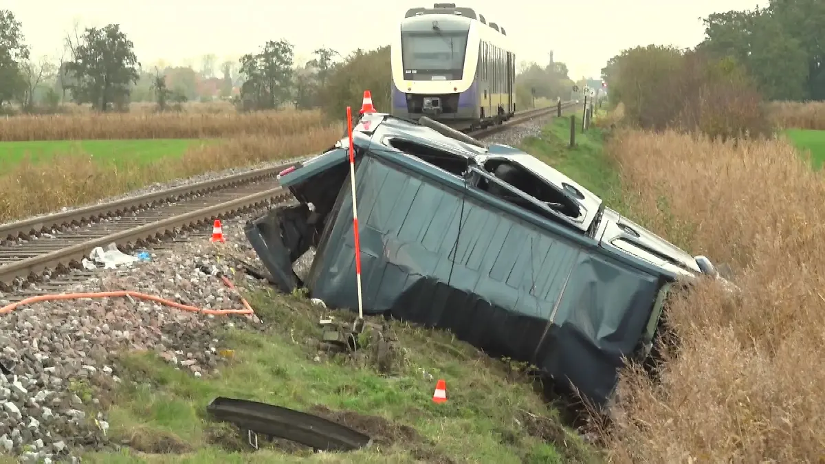 Der Nissan-Van liegt zerquetscht neben den Bahnschienen. Im Hintergrund ist der Zug zu sehen, der den Wagen gerammt hatte.