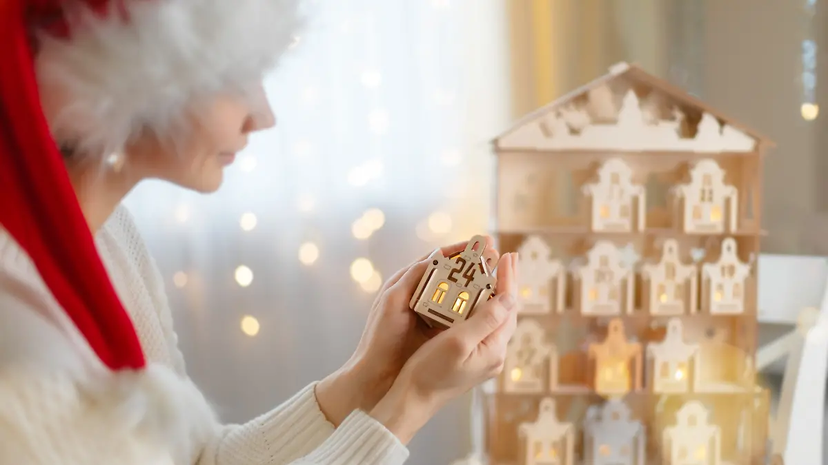 Frau mit Weihnachtsmütze öffnet Adventskalender.