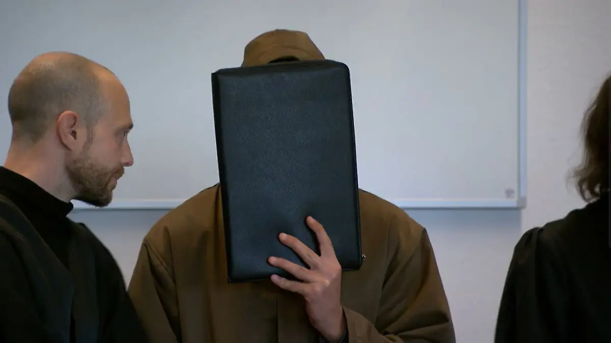 Einer der Angeklagten verdeckt sein Gesicht.