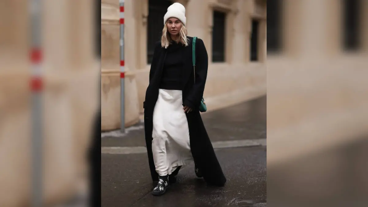Karin Teigl trägt zu ihrem weißen Satin-Rock von Mango einen scharzen Strickpulli und einen langen schwarzen Mantel