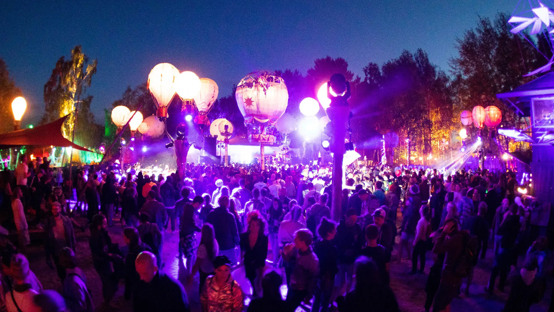 ARCHIV - 27.06.2019, Mecklenburg-Vorpommern, Lärz: Festivalbesucher tanzen auf einer mit leuchtenden Ballonen geschmückten Bühne auf dem Gelände des Fusion-Festival. In einer Woche soll in Lärz das Fusion-Festival 2023 beginnen. Die Veranstalter erwarten wieder mehrere zehntausend Gäste - und warnen vor Betrügern. (zu dpa "Fusion-Veranstalter warnen vor Betrug - 70 000 Gäste erwartet") Foto: Christian Charisius/dpa +++ dpa-Bildfunk +++
