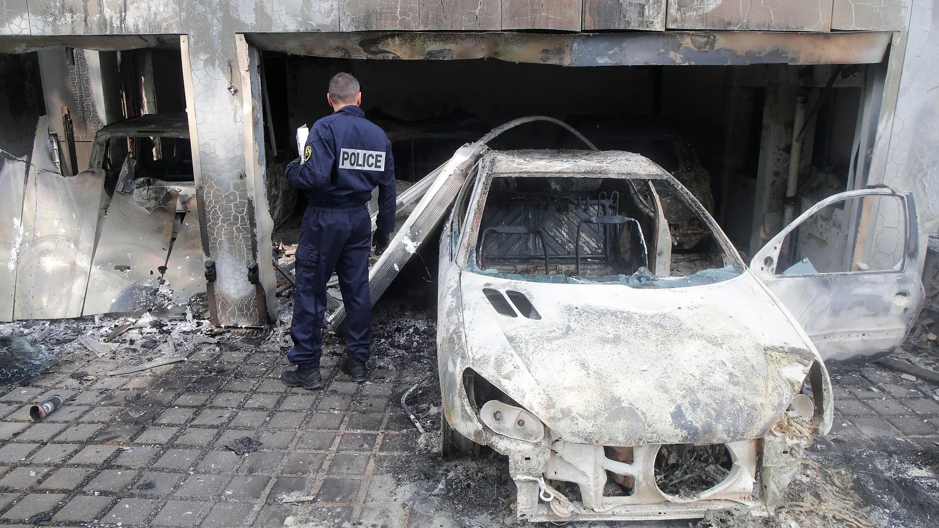 A police officer watches a charred car at the town hall of Mons-en-Barœul, northern France Thursday, June 29, 2023. Protesters angry after police shot a 17-year-old boy dead set cars and buildings ablaze in Paris suburbs. Unrest spread to some other French cities and towns Wednesday night and Thursday morning, despite increased security efforts and the president's calls for calm. (AP Photo/Michel Spingler)