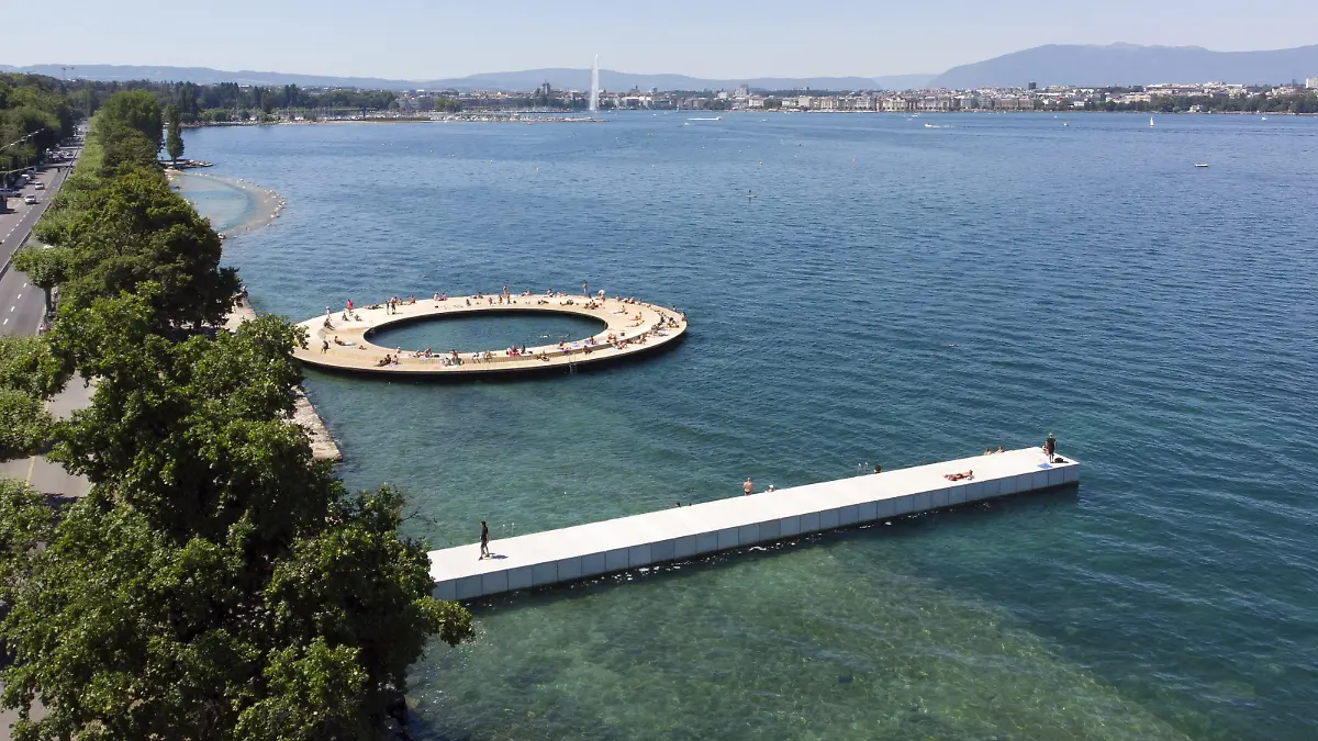 People enjoy the sunshine on new installations, a circular platform 40m in diameter and a pontoon on stilts 45m long, on the bank of the Geneva Lake with the famous water fountain "Le Jet d'Eau" and Cathedrale Saint Pierre are seen in background, in Cologny near Geneva, Switzerland, Sunday, July 19, 2020. The canton of Geneva and the city of Cologny open since this week end a new space, a circular platform 40m in diameter and a pontoon on stilts 45m long, for the bathing into the Geneva lake. (KEYSTONE/Salvatore Di Nolfi)