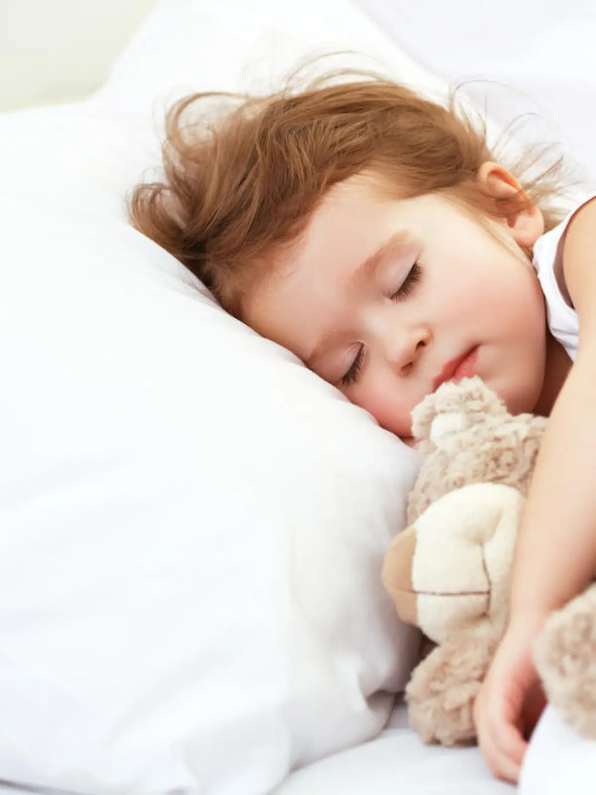 child little girl sleeps in the bed with a toy teddy bear
