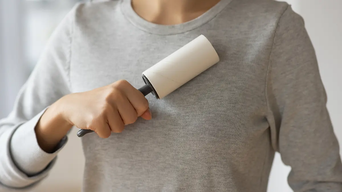 Frau hält Fusselrolle an Pullover.