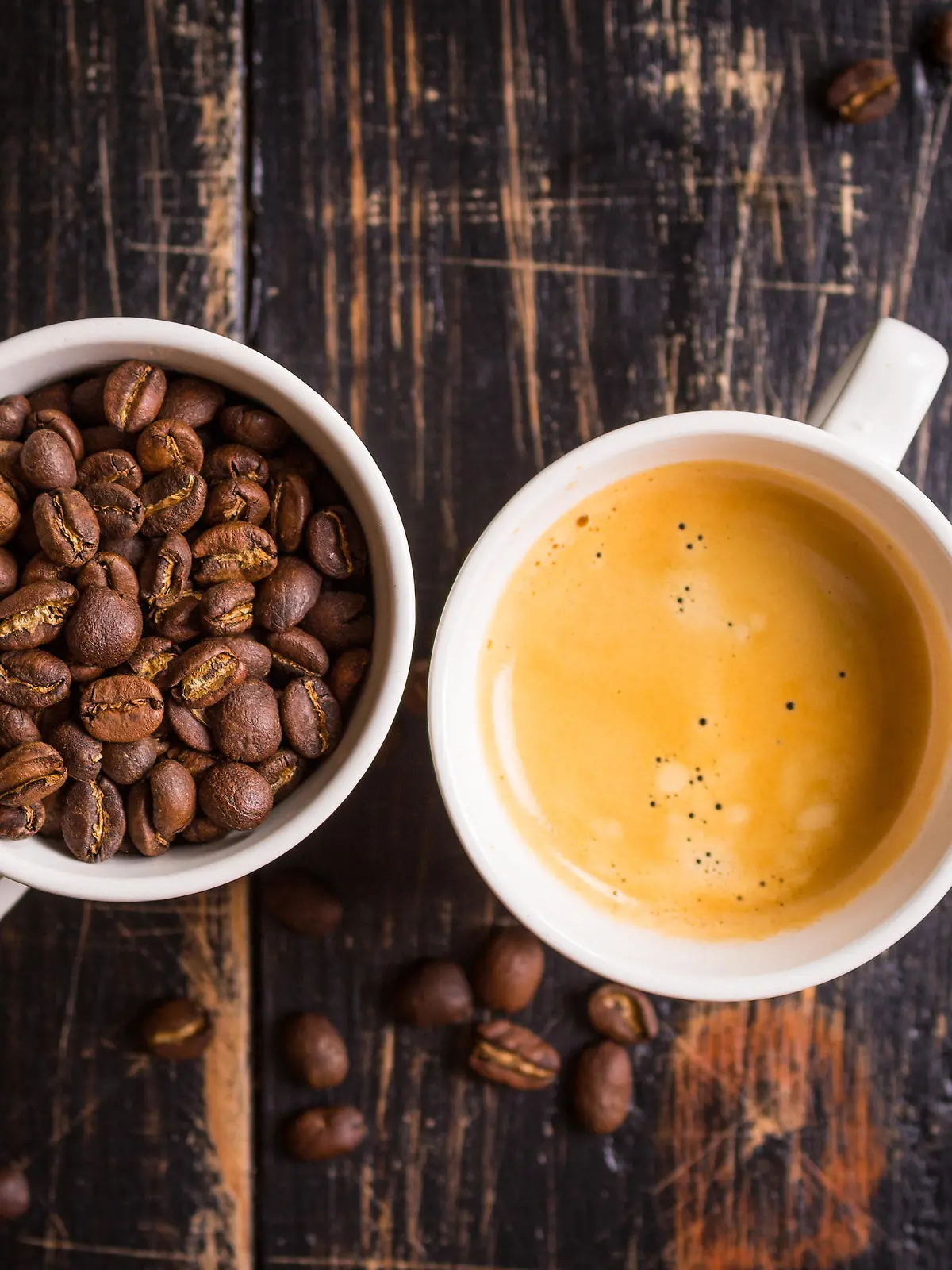 Fresh espresso and whole roaster coffee beans in a white cups on old dark wooden textured table