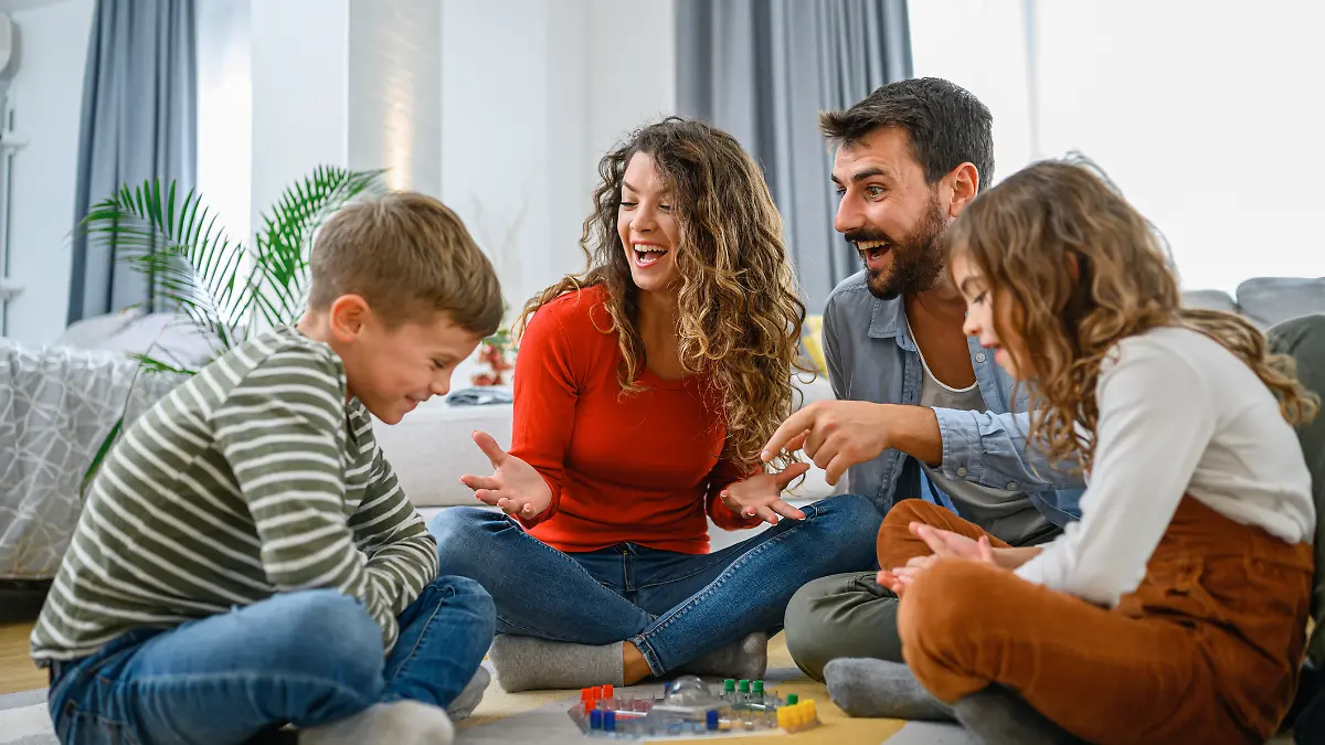 Eine junge Familie mit zwei Kindern sitzen auf dem Boden und spielen Gesellschaftsspiele.