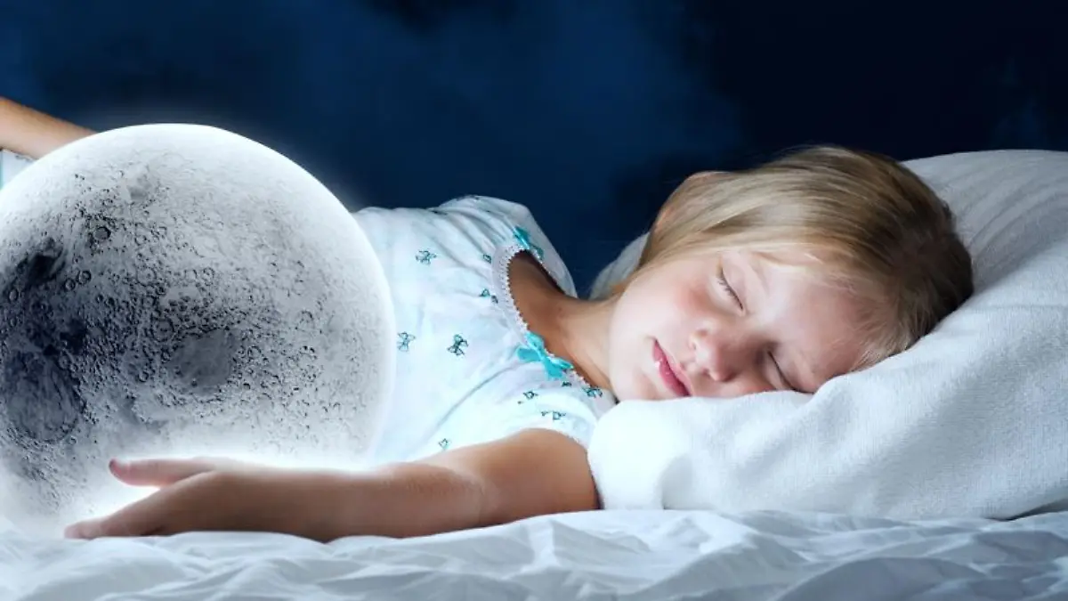 Kind liegt mit geschlossenen Augen im Bett und hat eine Hand auf einem leuchtenden Globus mit LED-Licht.