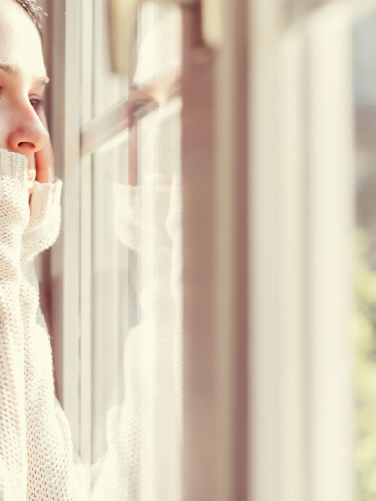 Eine Frau blickt nachdenklich aus dem Fenster. Sie scheint traurig zu sein.