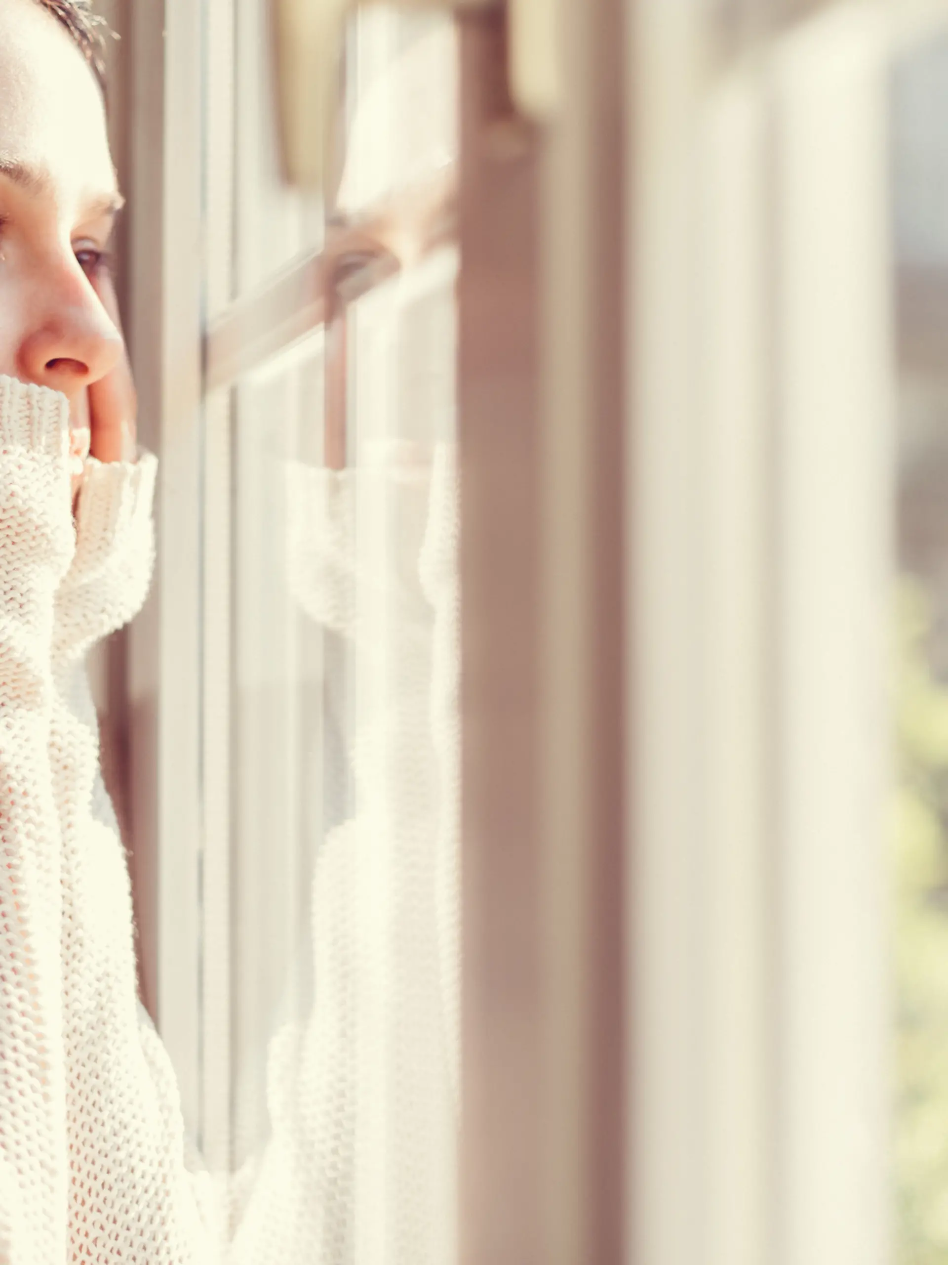 Eine Frau blickt nachdenklich aus dem Fenster. Sie scheint traurig zu sein.