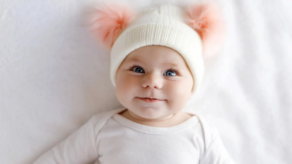 Cute adorable baby child with warm white and pink hat with cute bobbles. Happy baby girl on white background and looking at the camera. Close-up for xmas holiday and family concept.