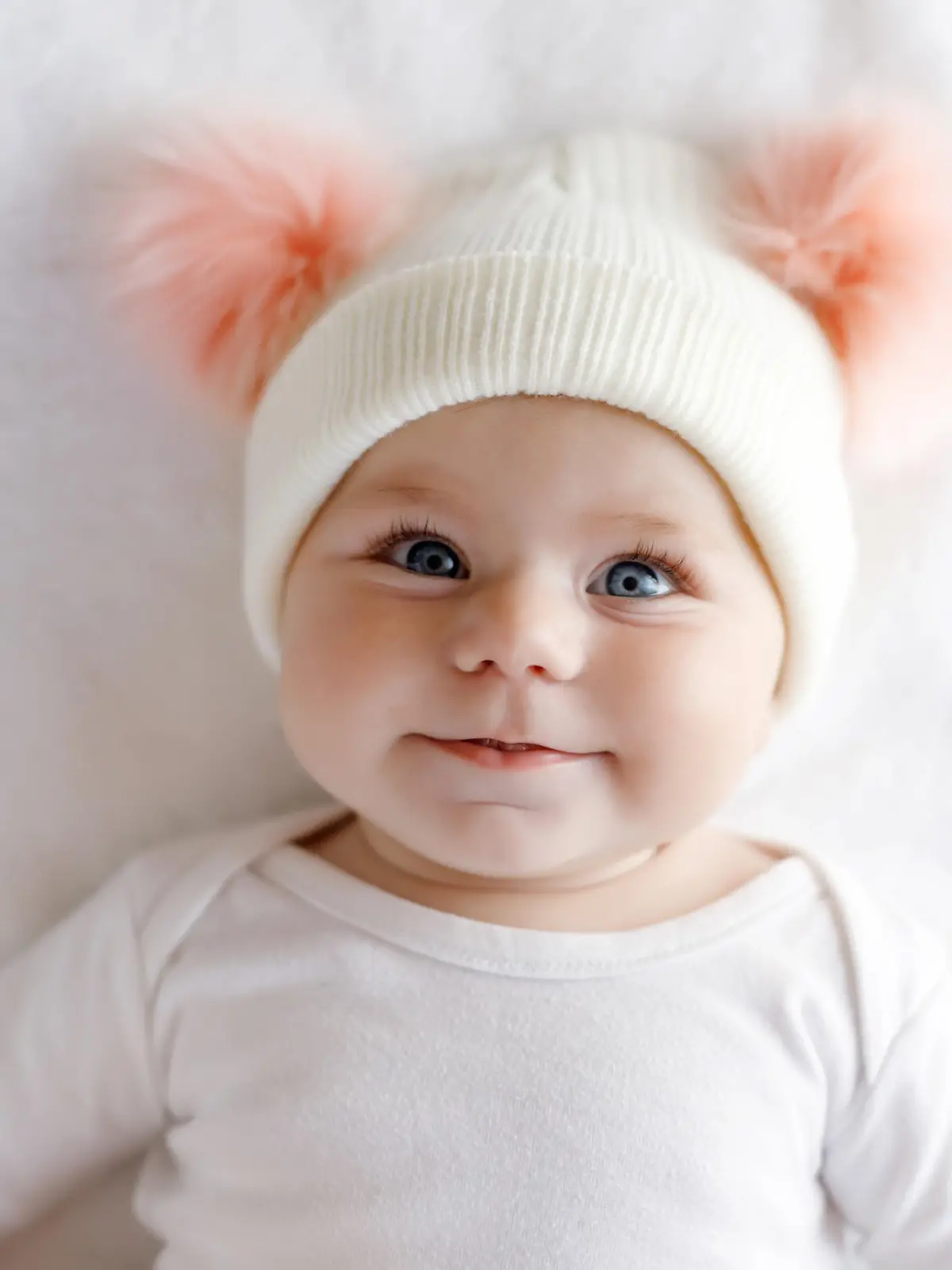 Cute adorable baby child with warm white and pink hat with cute bobbles. Happy baby girl on white background and looking at the camera. Close-up for xmas holiday and family concept.